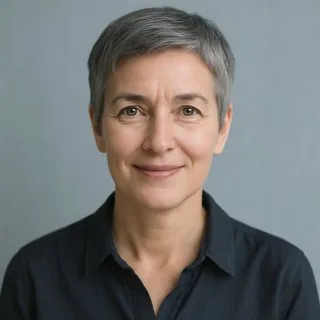 Portrait einer Frau Anfang 50 mit kurzen grauen Haaren und schlichter dunkler Bluse, freundlicher Blick in die Kamera